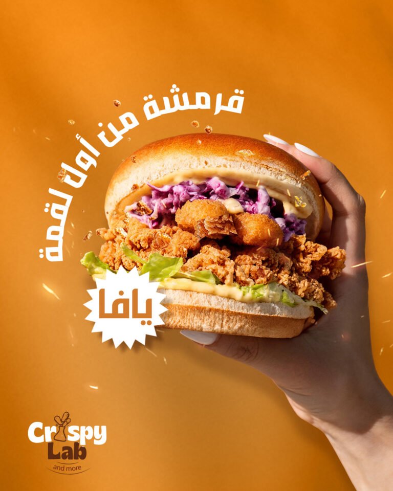A hand holding the Yafa fried chicken burger, stacked with red cabbage slaw and sauce, on a warm orange ground.